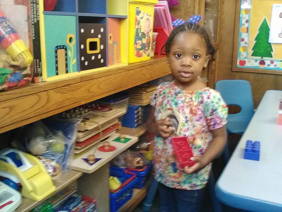 Child holding a red building block in a classroom