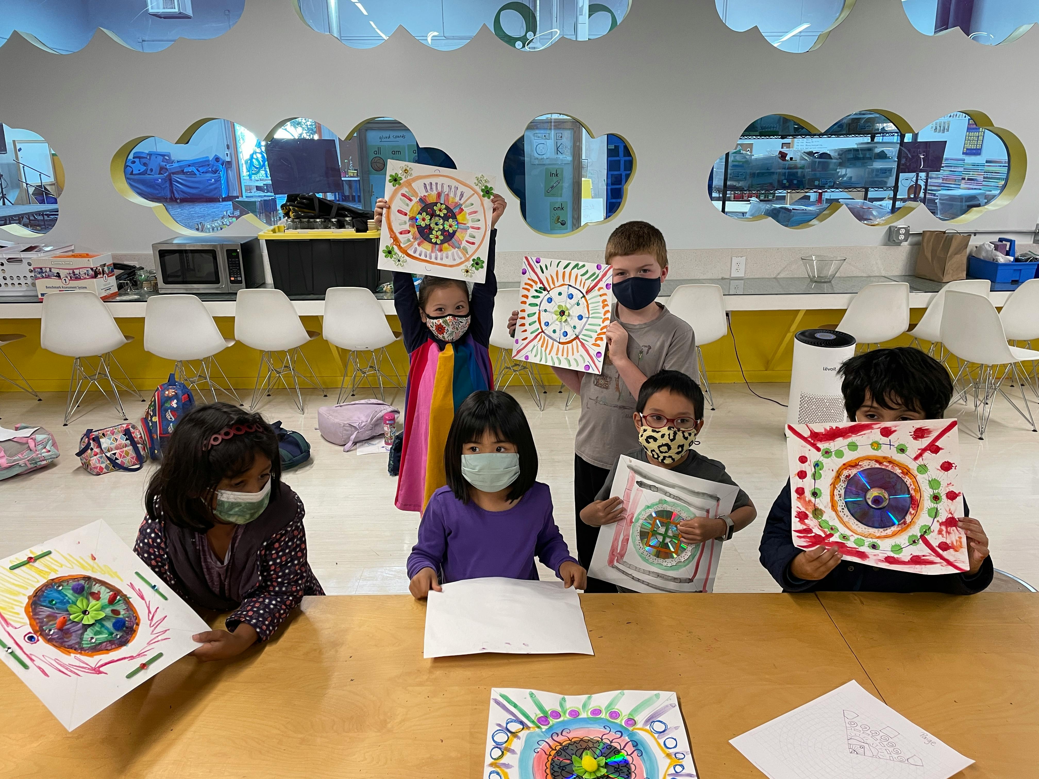 Children in masks holding up colorful artwork in-progress art projects