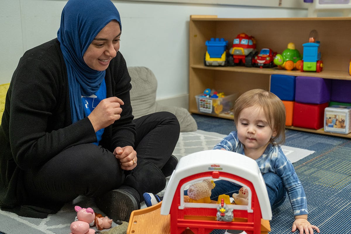 Person in hijab and child playing with a toy barn on the floor