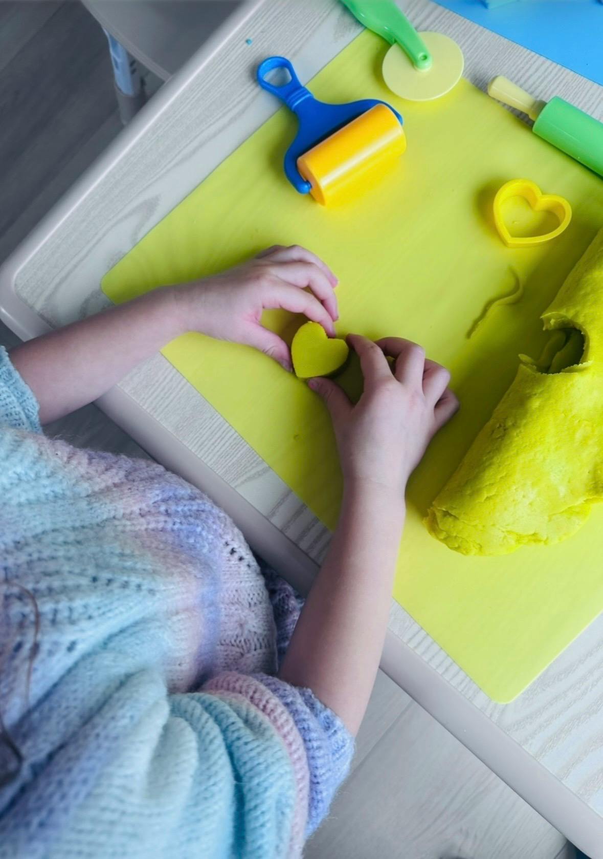 Child shaping yellow dough with a heart cutter on a table