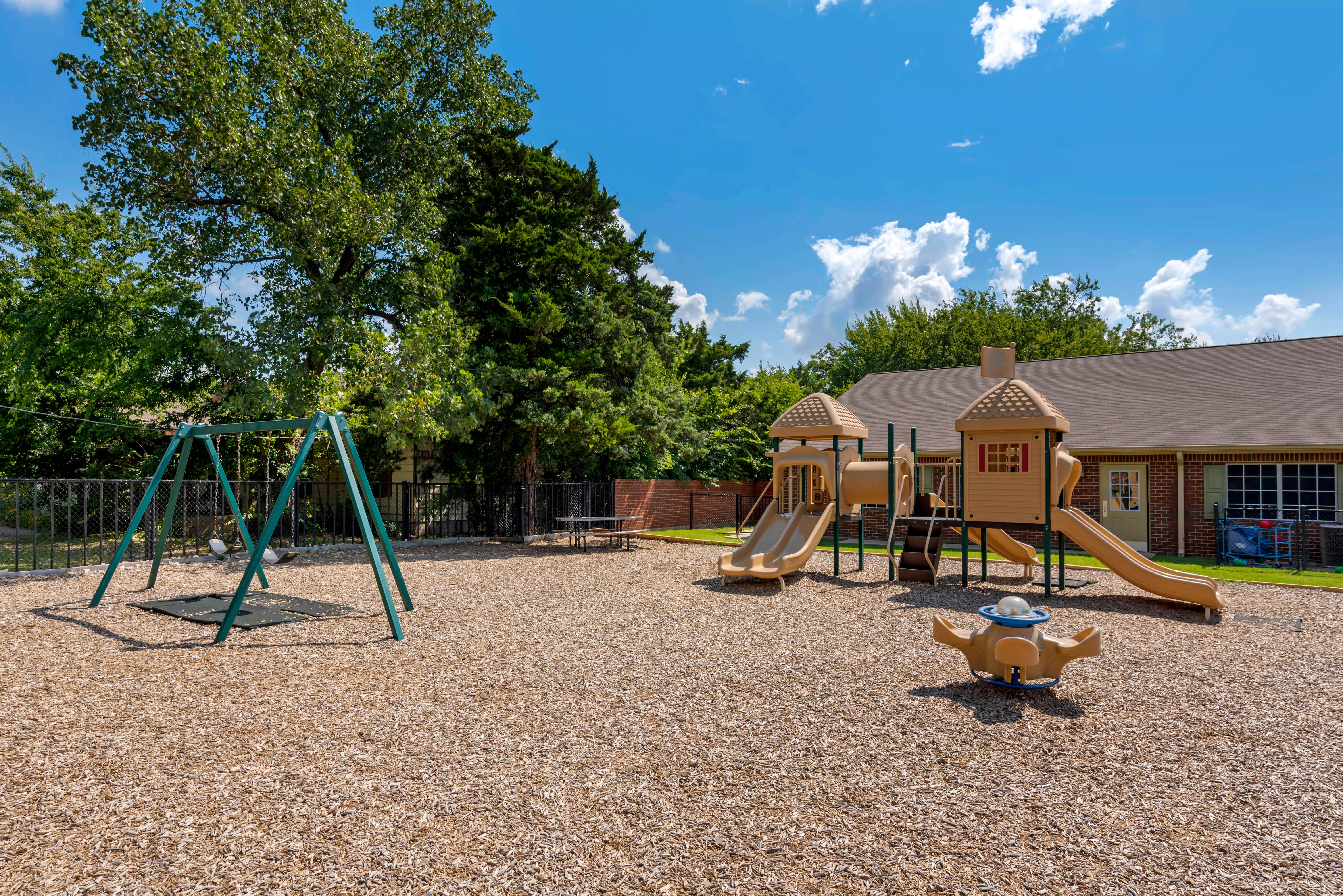 Playground with swing set, slides, and wood chips on the ground