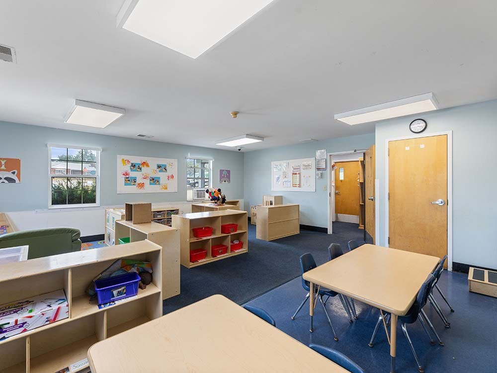Empty classroom with small tables and chairs, shelves, and windows