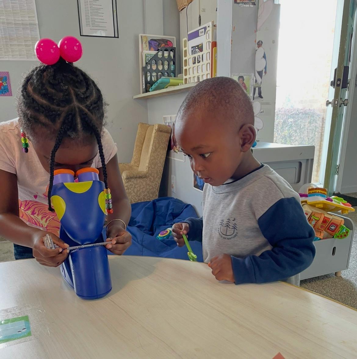 Child looking through a blue toy microscope next to another child