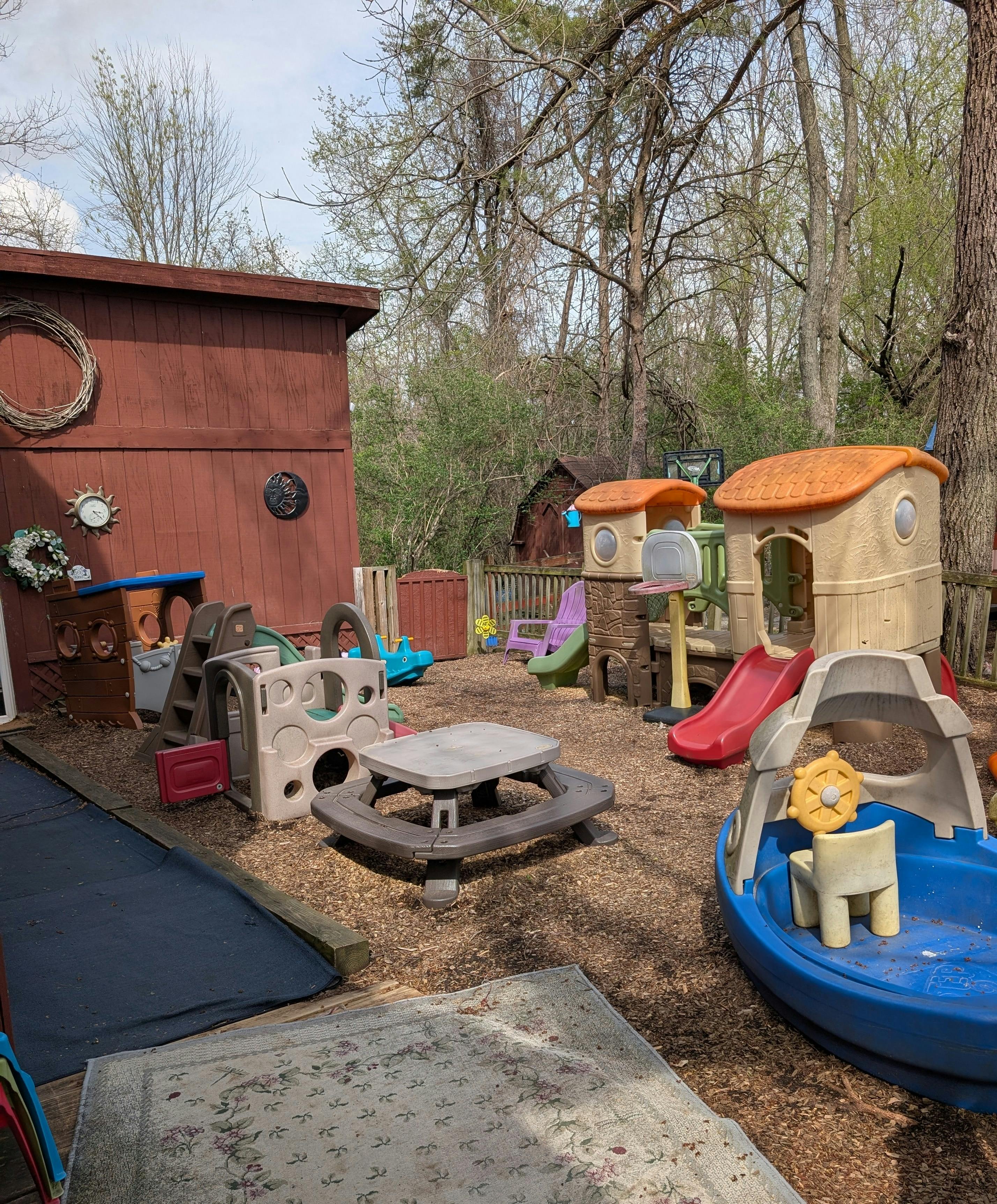 Outdoor children's play area with slides, playhouses, and a small table on wood chips