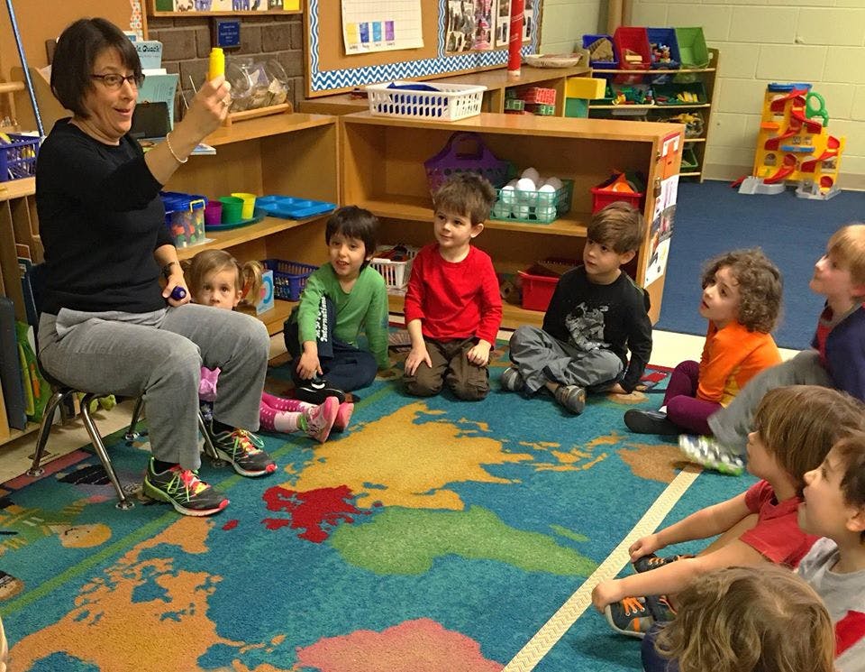 Person sitting in a chair holding up an object to a group of children