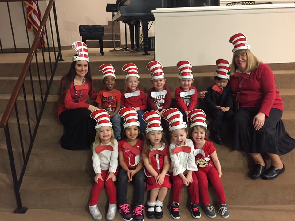 Two people and multiple children wearing red and white striped hats