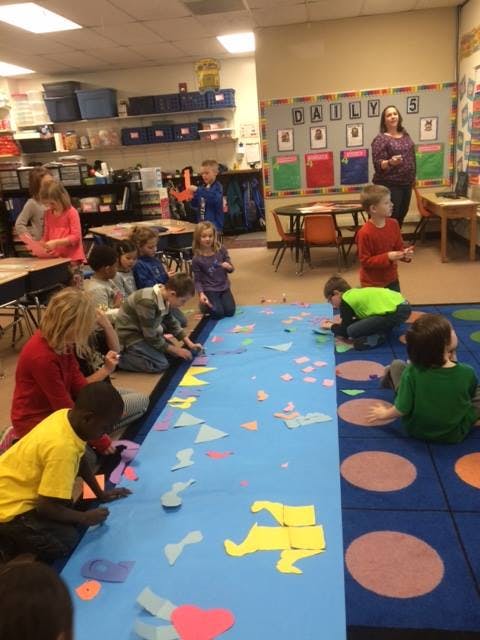 Children and an adult in a classroom, children working on a blue mat with cutouts