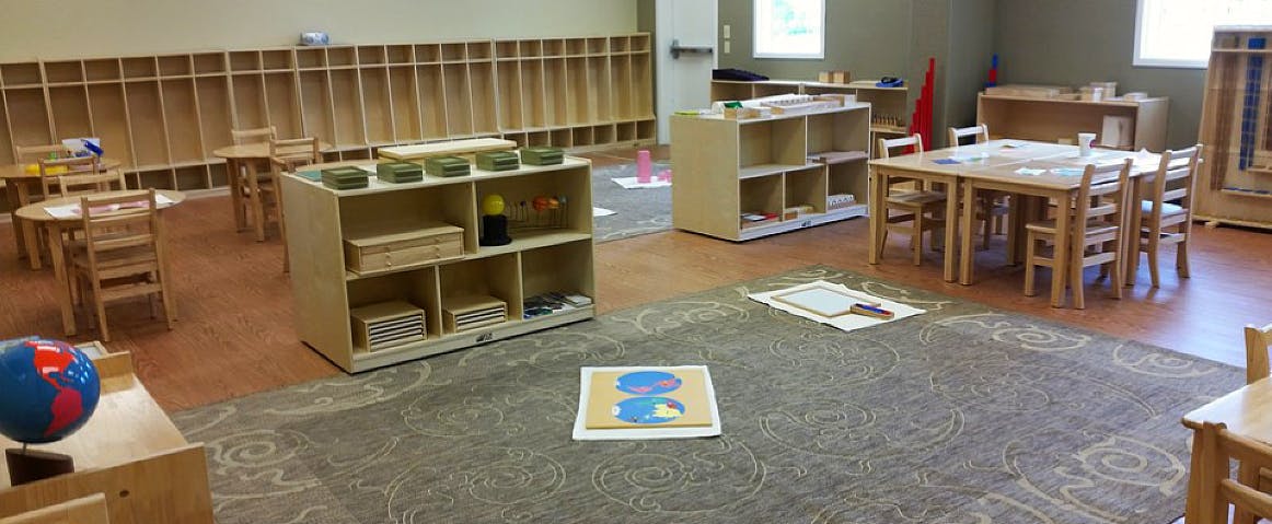 Empty classroom with small tables, chairs, and shelves