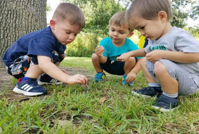Three children crouching in grass, looking at the ground