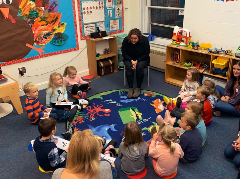 Adult sitting on a chair with children sitting on a rug in a circle
