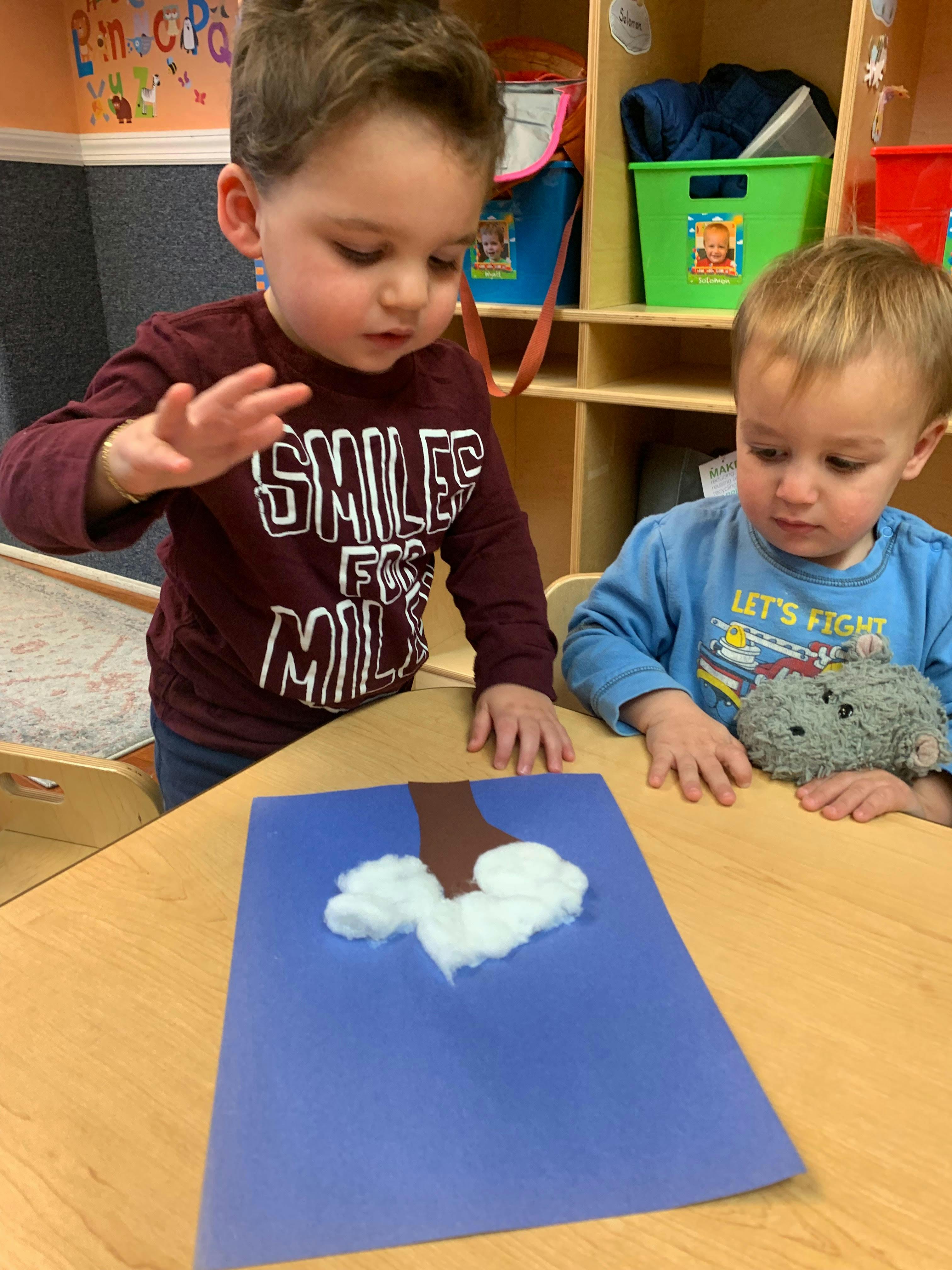 Two children looking at a craft project with cotton balls on blue paper