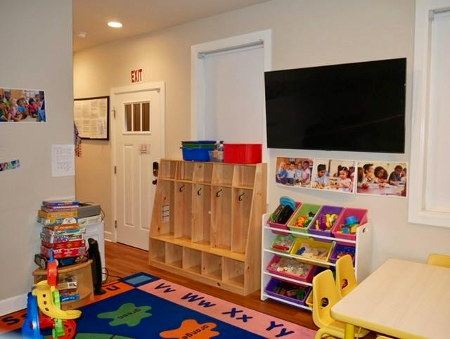 Classroom with toy storage units, alphabet rug, table, and wall-mounted screen