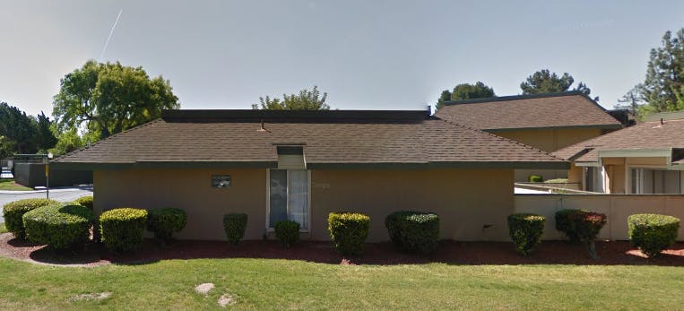 Single-story building with a brown roof and bushes in front of it green bushes