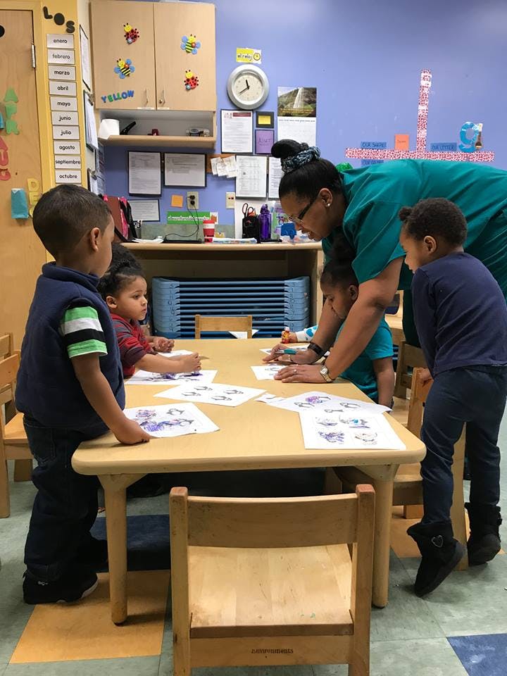 Adult and children drawing at a table in a classroom