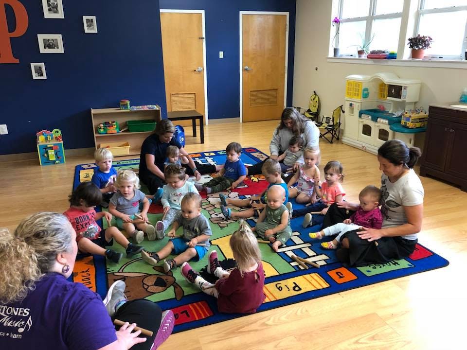 Adults and children sitting on a colorful rug in a classroom