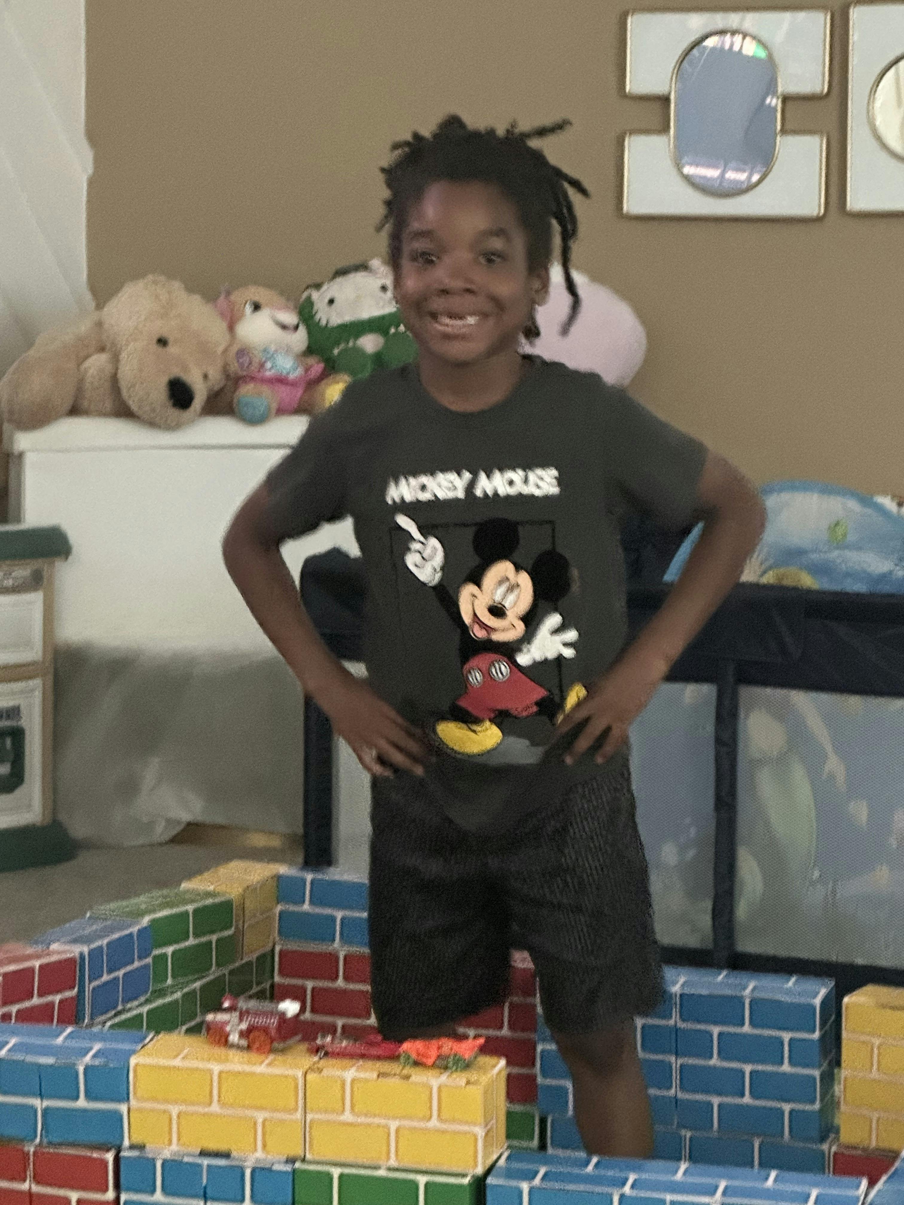 Child wearing a Mickey Mouse shirt standing inside a toy brick structure