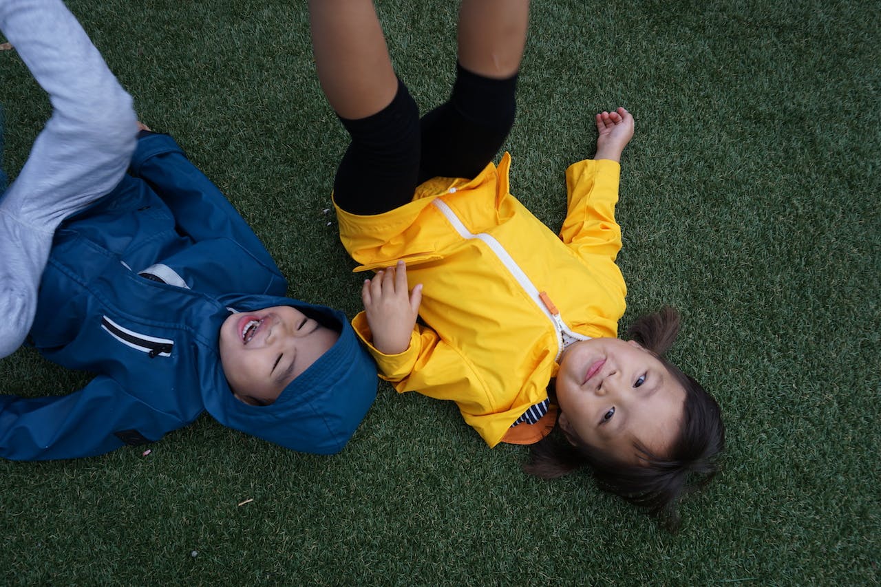 Two children lying on green grass, one in blue and one in yellow