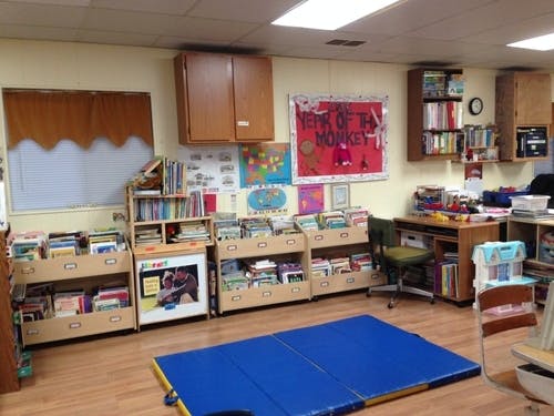 Classroom with bookshelves, a desk, and a blue mat on the floor