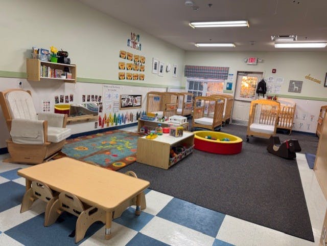 Classroom with cribs, play area with a rug, and a small table with chairs