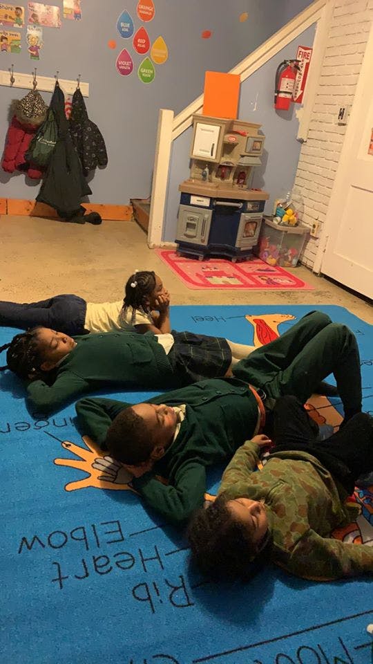 Four children lying on a blue rug in a classroom