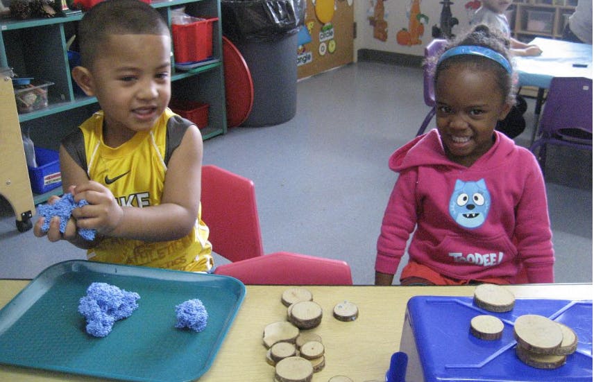 Two children playing with materials at a table in a classroom