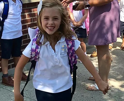 Child wearing a white shirt with a cross and a backpack