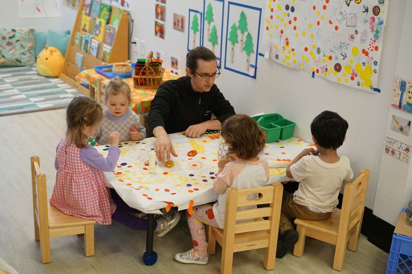 Man and three children doing an art project at a table in a classroom