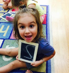 Child holding a small chalkboard with the letter S drawn on it
