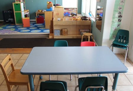 Classroom with a table and chairs in the foreground, toys and shelves in the background