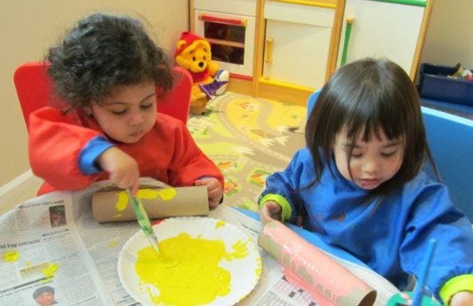 Two children painting cardboard tubes at a table