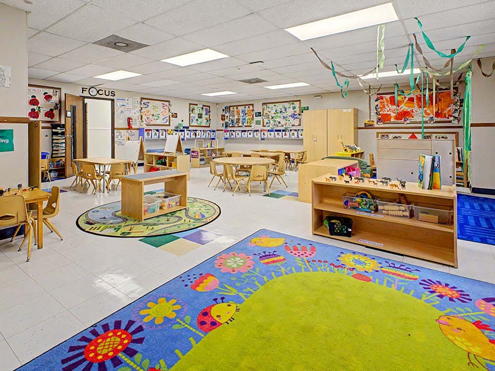 Empty classroom with small tables and chairs, colorful rugs, and decorations
