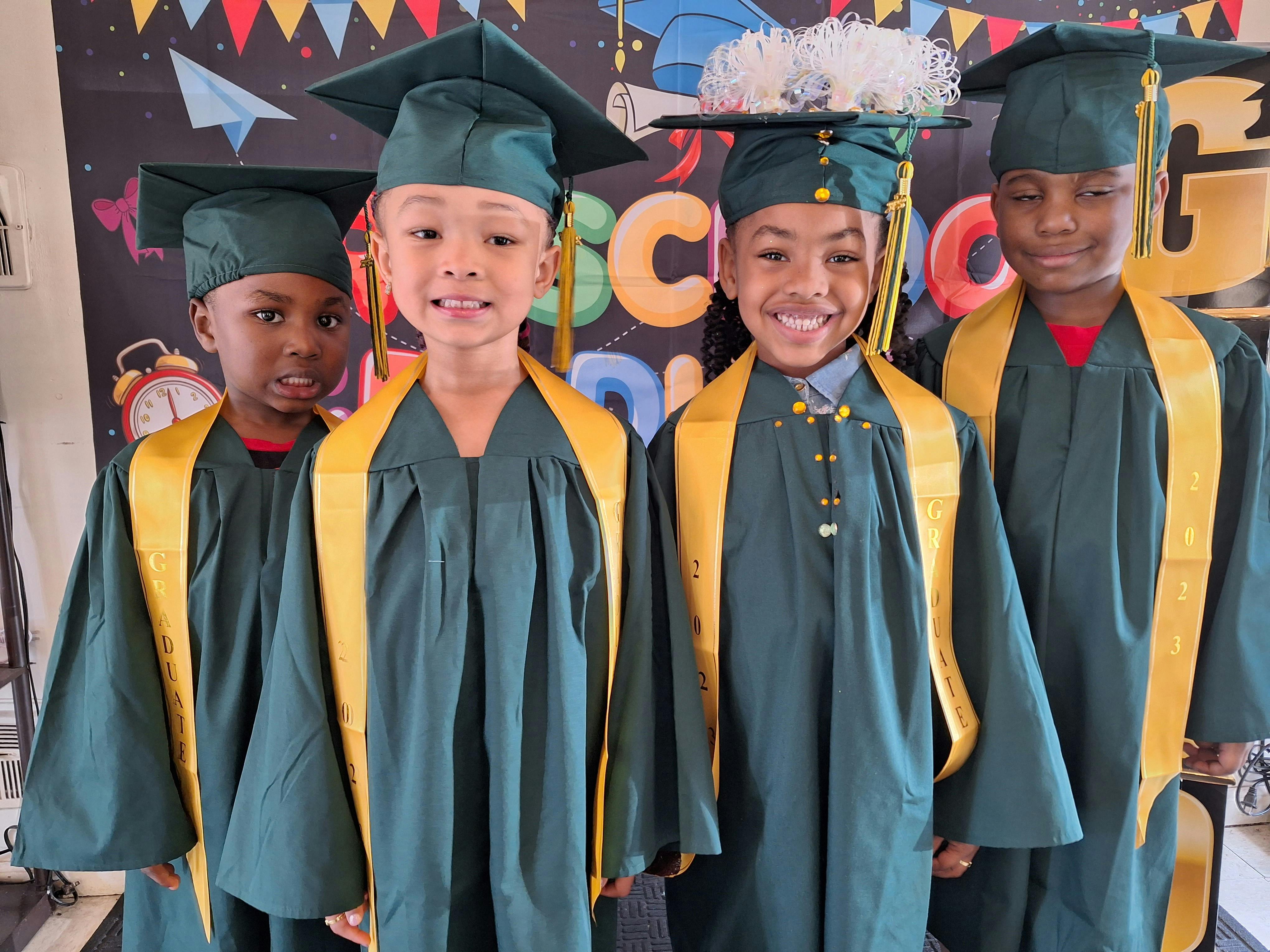 Four children in green graduation caps and gowns with yellow sashes