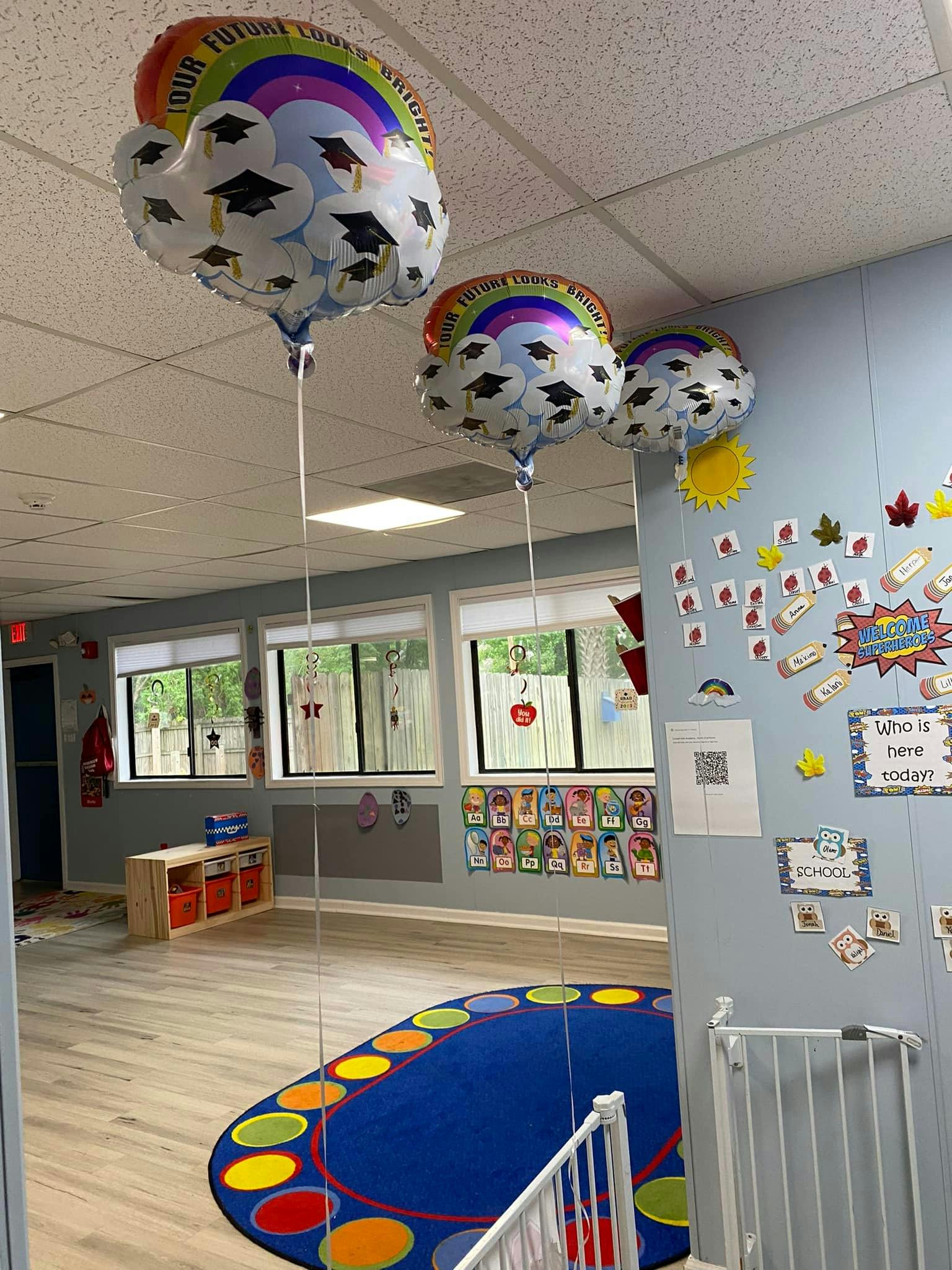 Classroom decorated with graduation balloons, colorful rug, and child's artwork