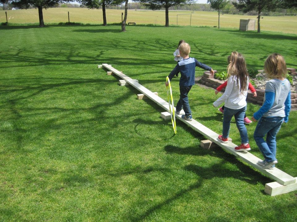 Children walking on a wooden balance beam outdoors