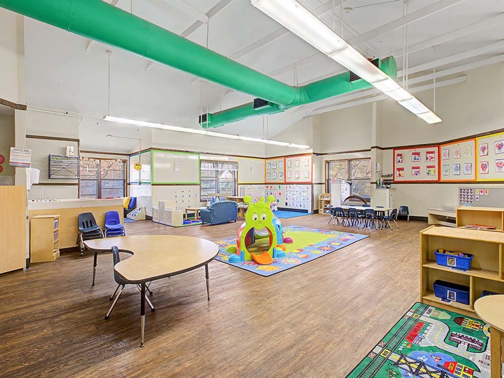 Classroom with child-sized tables and chairs, play mats, and learning displays