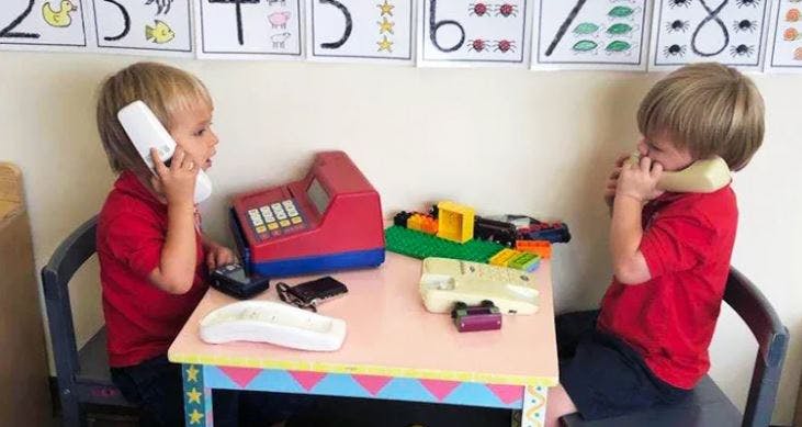 Two children playing with toy phones at a small table