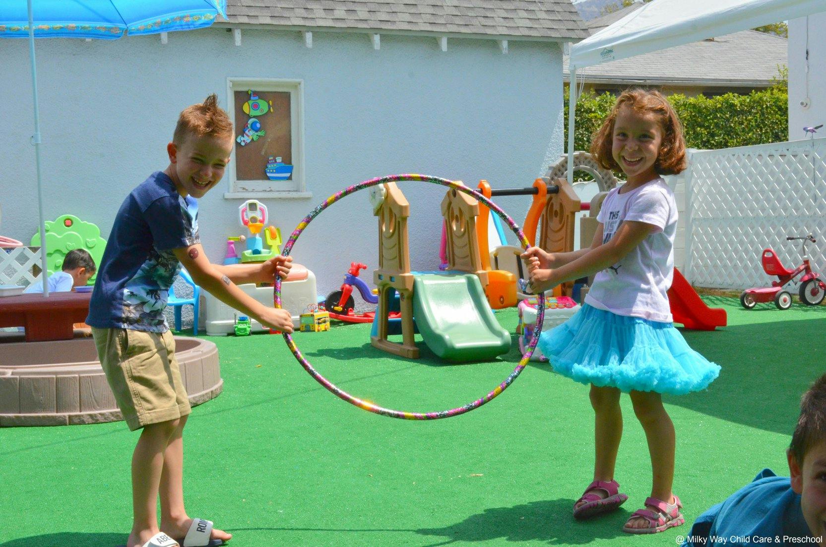 Two children holding a hula hoop on a playground