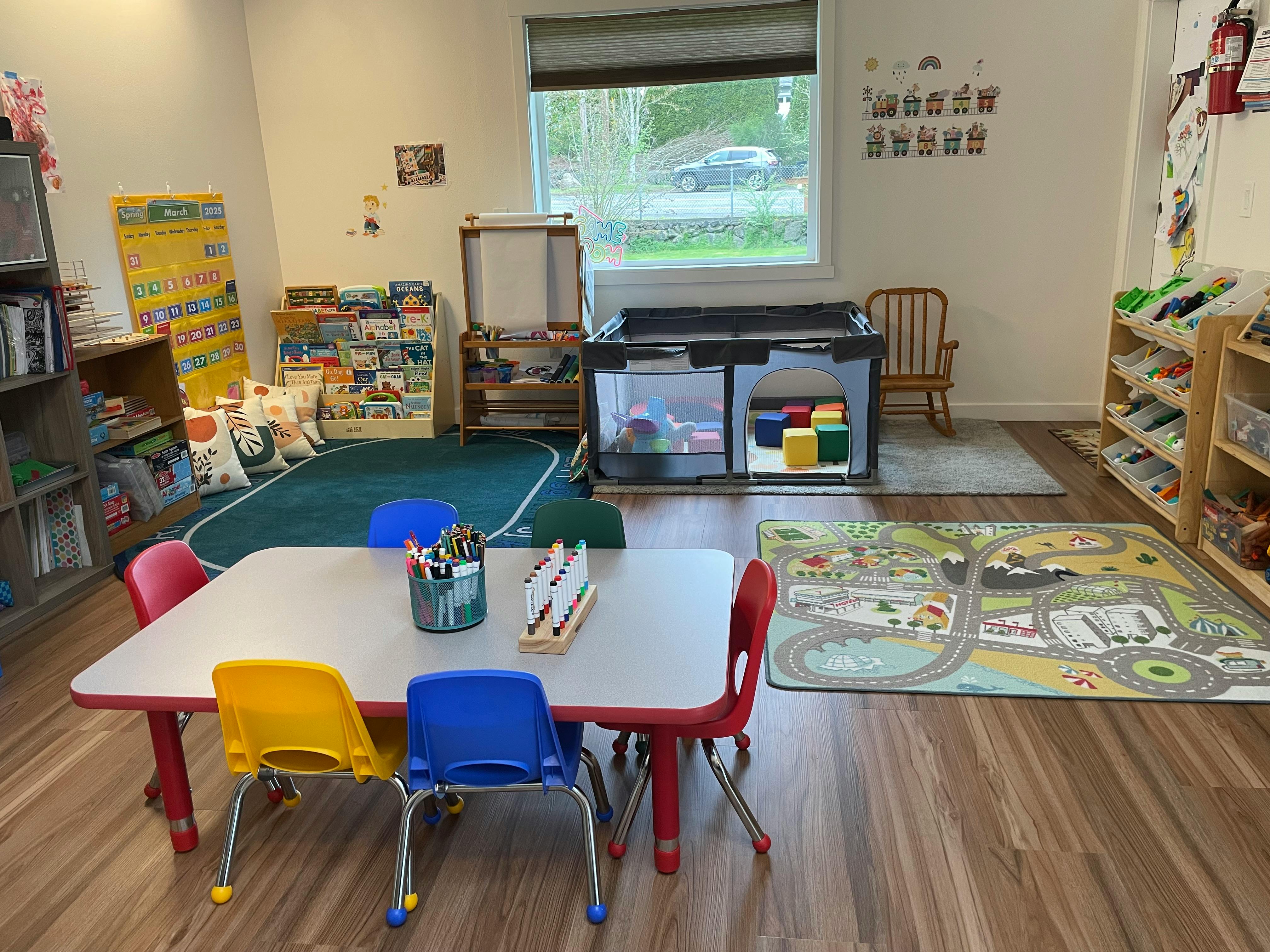 Classroom with small tables and chairs, play mats, and storage shelves