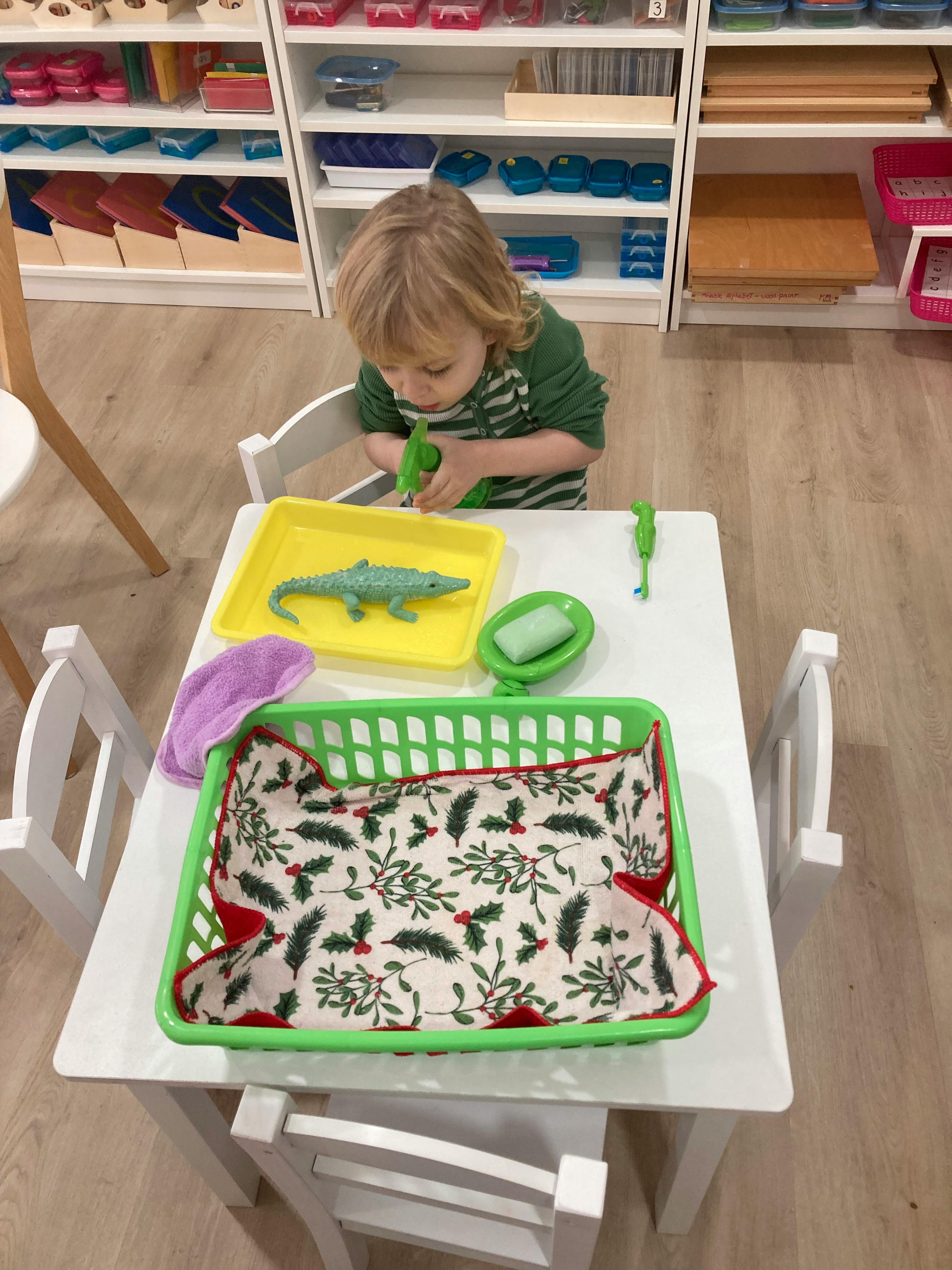 Child playing with a toy alligator and brush at a table