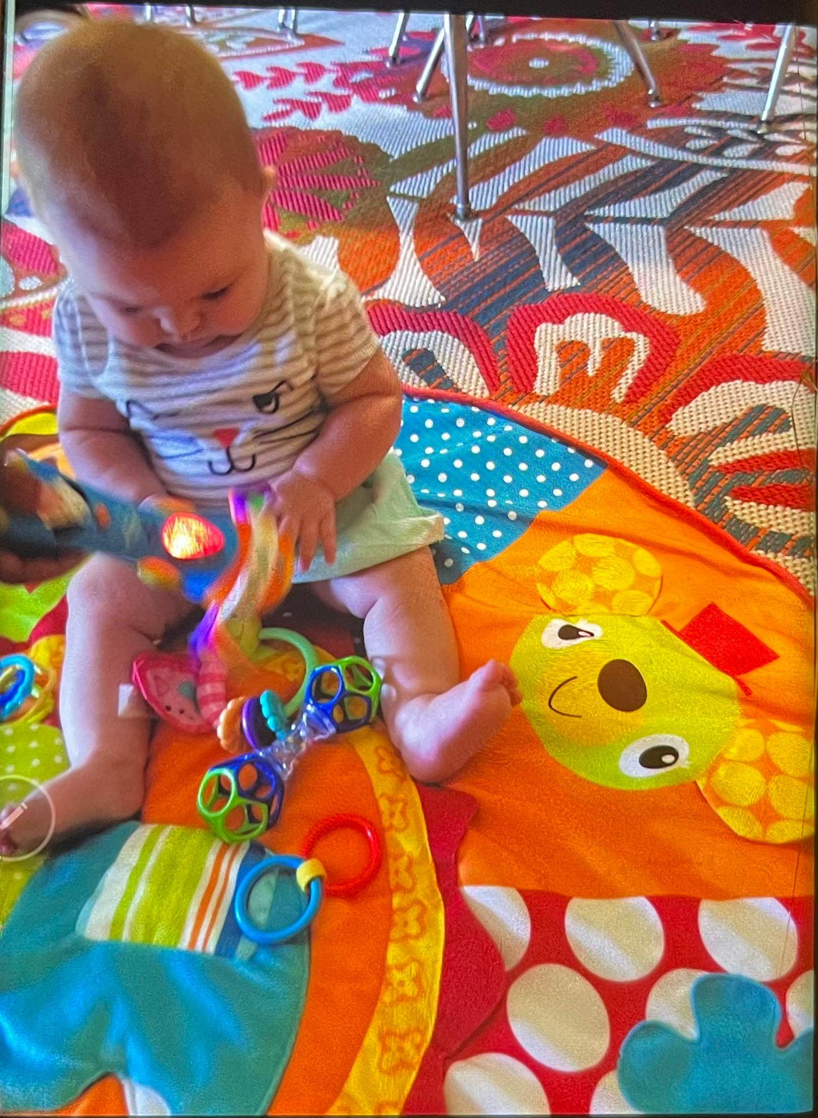 Child sitting on a playmat, holding a toy