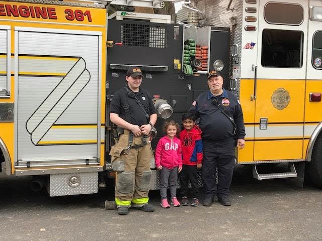 Two firefighters standing with two children in front of a fire truck