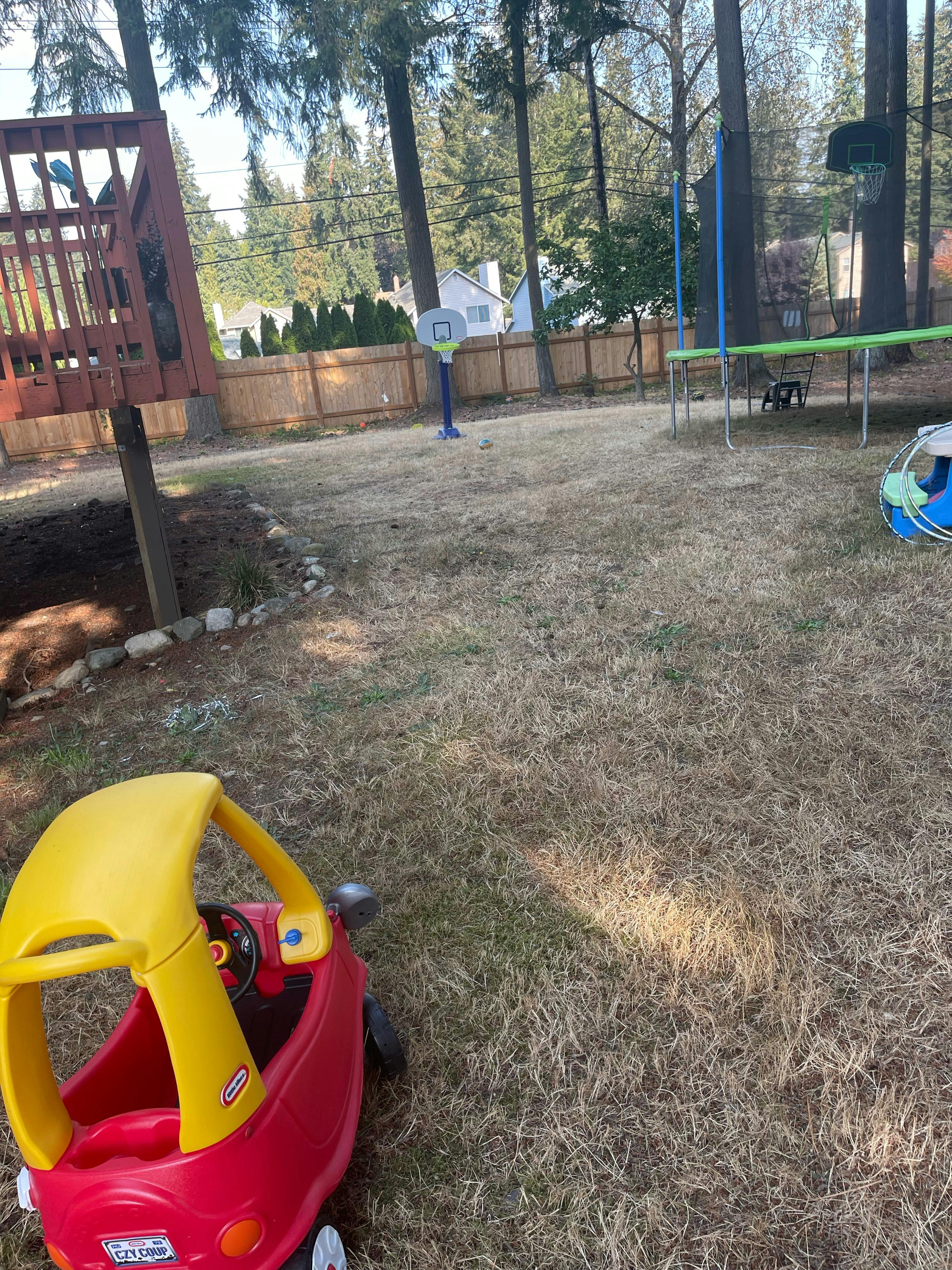 Red and yellow toy car in a backyard with a trampoline and basketball hoop