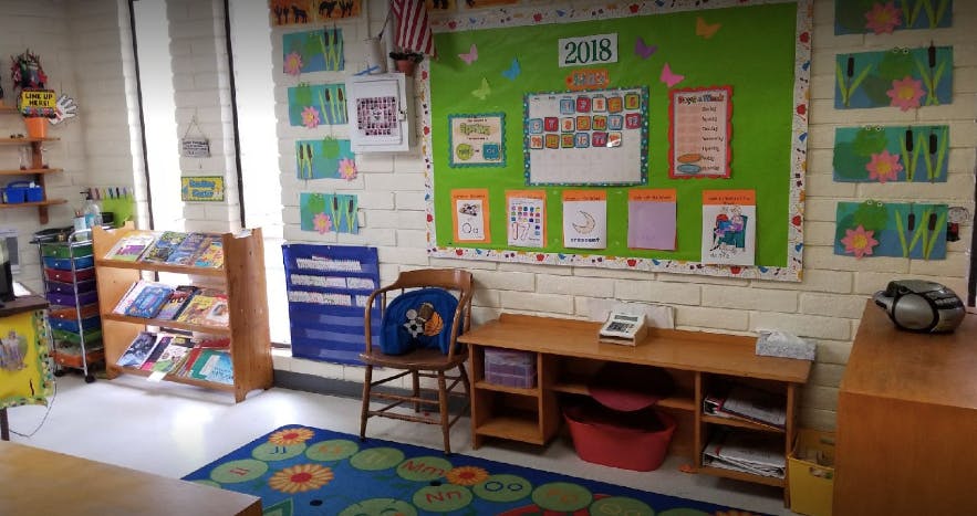 Classroom with a green bulletin board, small wooden desk, and book display