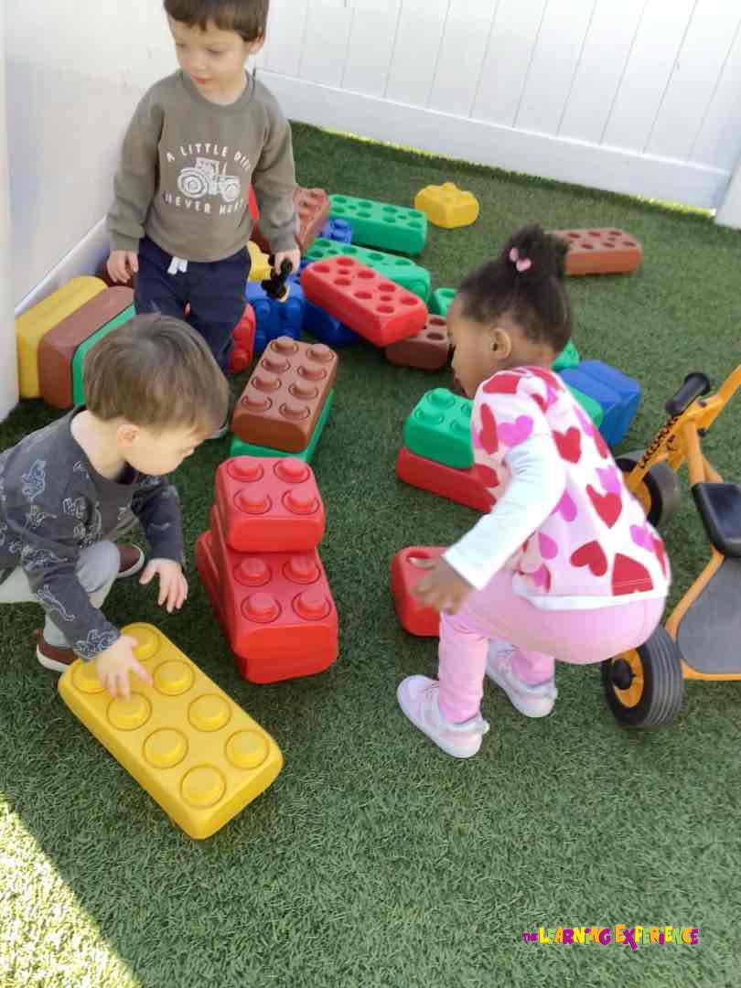 Three children playing with oversized interlocking blocks on artificial grass
