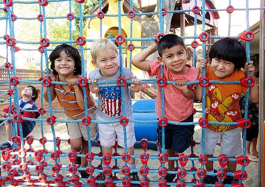 Four children smiling through a climbing net