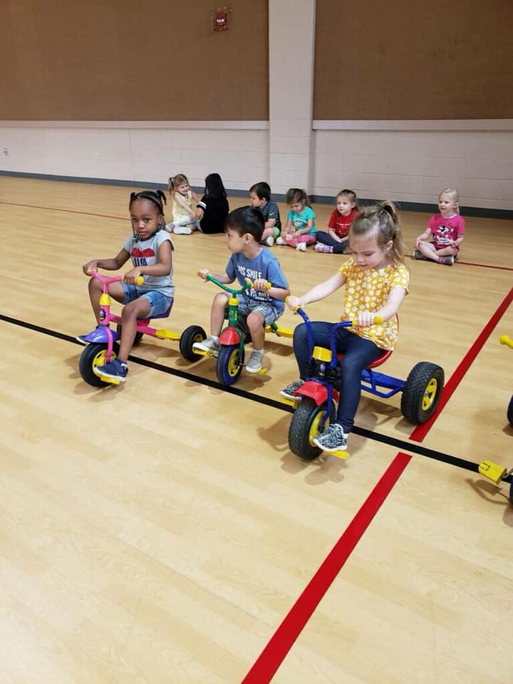 Children riding tricycles in a gym