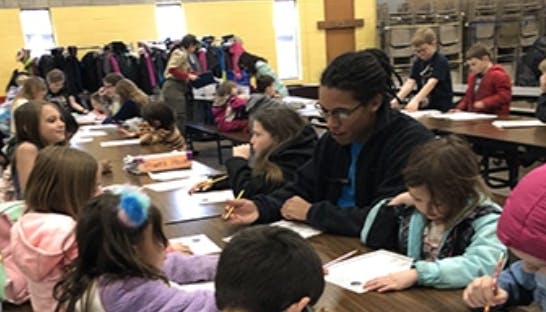 Adult and children seated at tables, writing