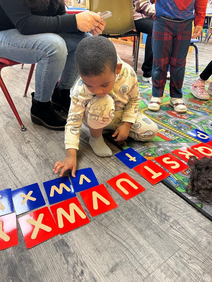 Child crouching on floor, playing with alphabet letter tiles