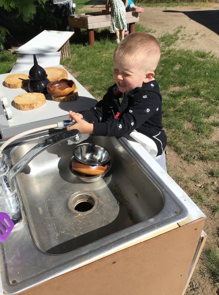 Child playing with a water hose at an outdoor sink