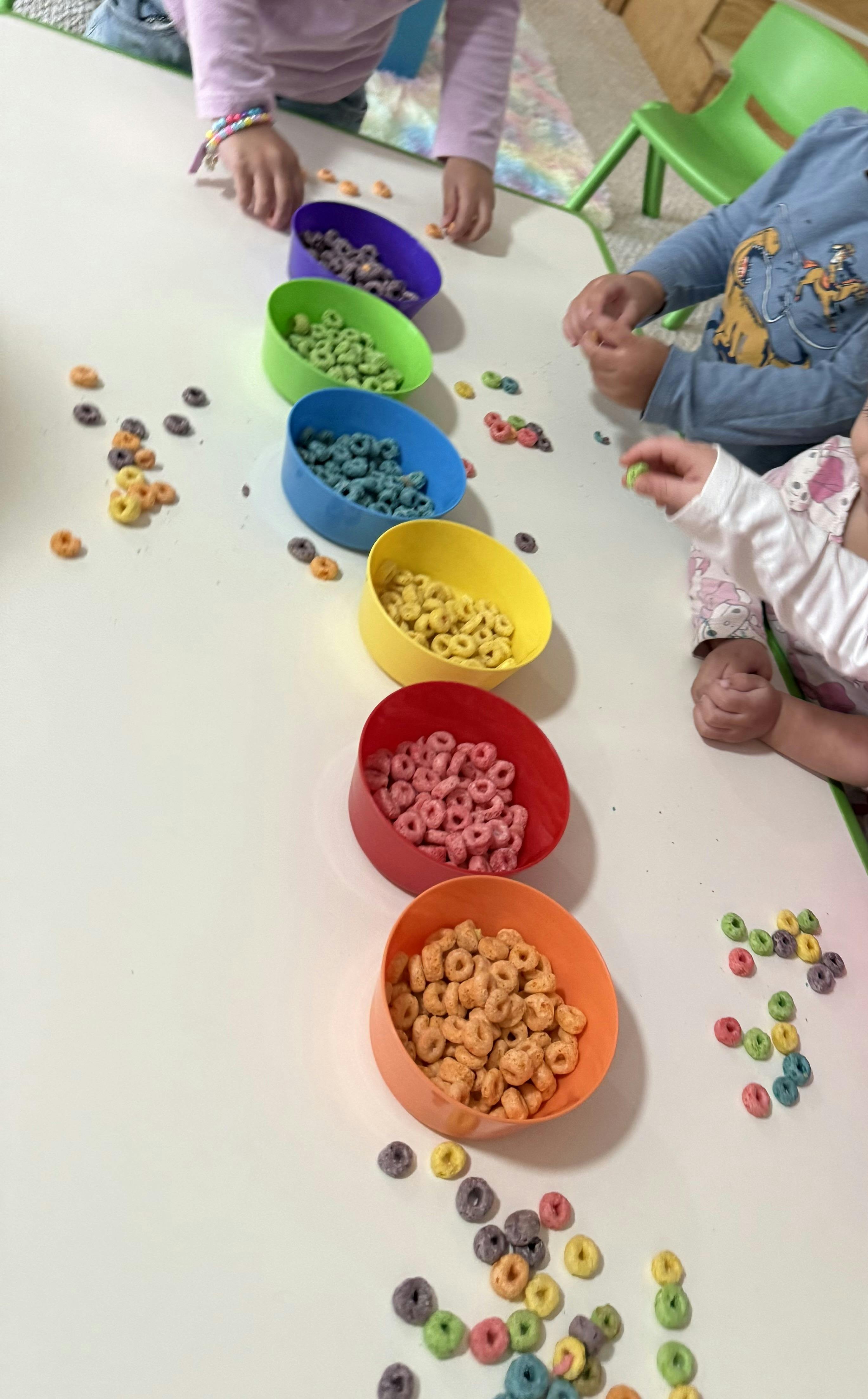 Children sorting colorful cereal into matching colored bowls
